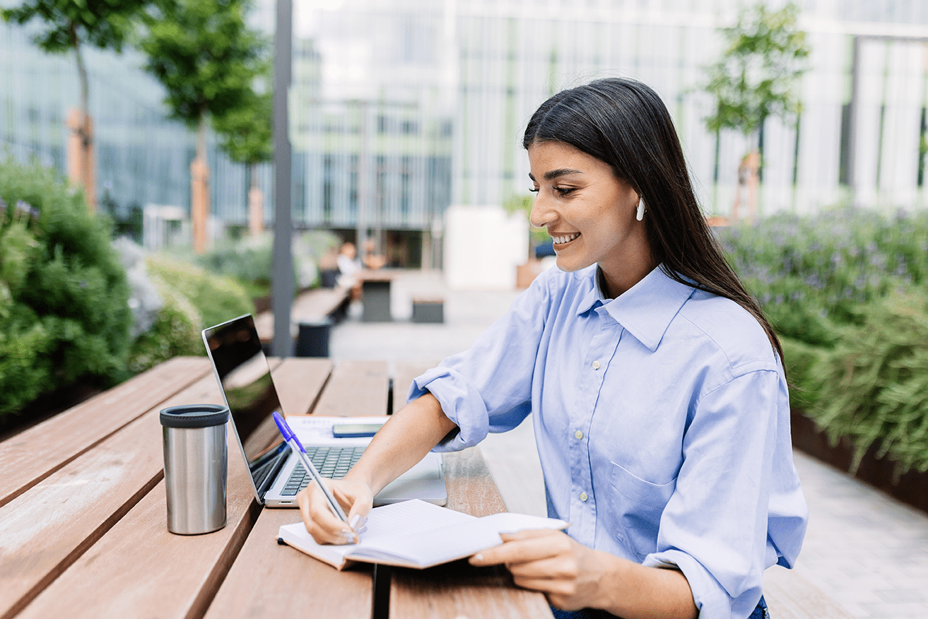 Happy adult student learning online using laptop sitting outside at campus college